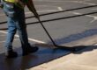 Construction worker uses sealcoating brush on asphalt pavement project