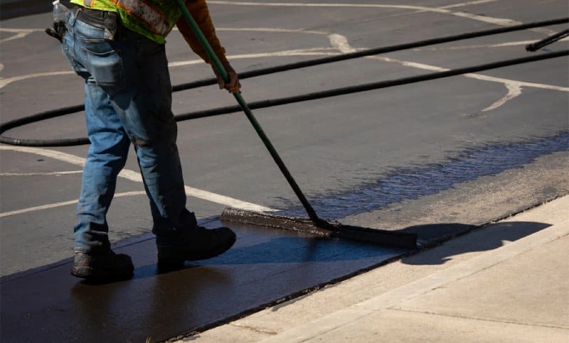 Construction worker uses sealcoating brush on asphalt pavement project