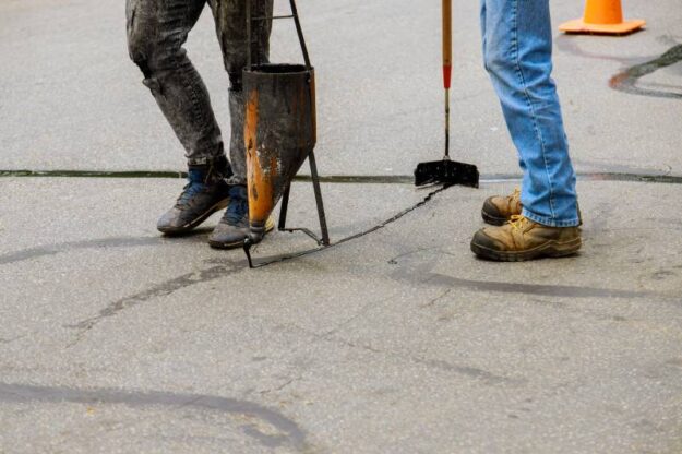 Two construction workers apply sealcoat to asphalt road.