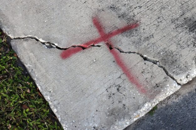 Concrete sidewalk marked with red "X" for repair.