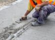 Construction worker smoothing out fresh concrete on sidewalk.