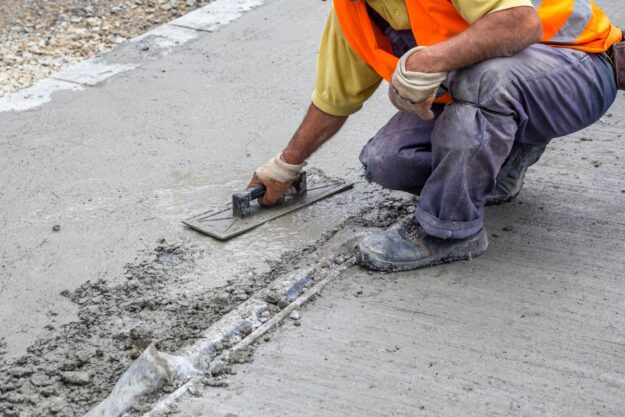 Construction worker smoothing out fresh concrete on sidewalk.